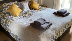Un lit bien fait, avec une literie à motifs floraux, deux oreillers et des serviettes pliées, posé sur un plancher en bois.