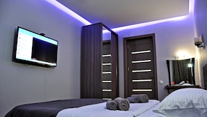 Ein modernes Hotelzimmer mit Bett, Flachbildfernseher an der Wand, Kleiderschrank und beleuchtetem Spiegel.