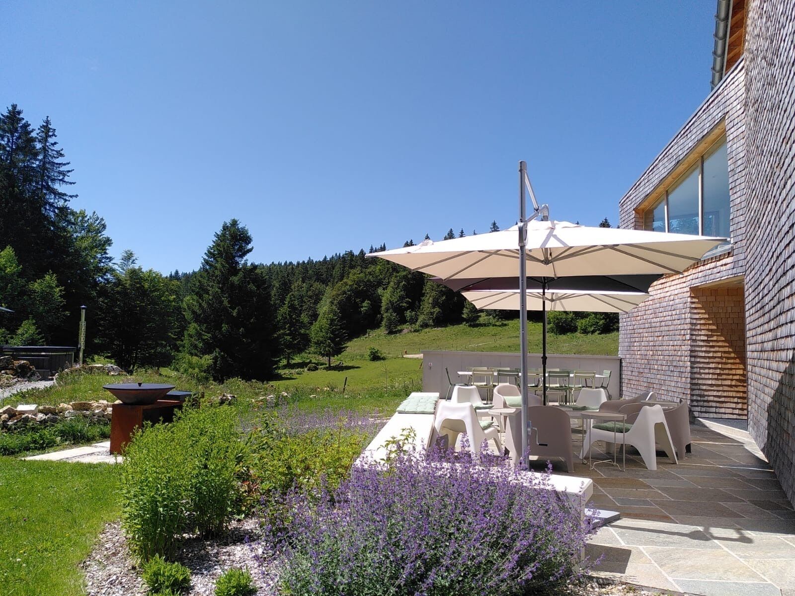 An outdoor patio area with a table and chairs, surrounded by a garden with lavender plants.
