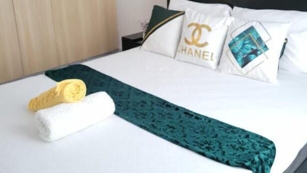 A neatly made bed with white linens, a green throw blanket, and pillows with a Chanel logo. - Lux Suites Supaboma Apartments Embakasi (Nairobi)