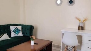A living room with a green sofa, a wooden coffee table, a white desk, and a small potted plant. - Lux Suites Supaboma Apartments Embakasi (Nairobi)