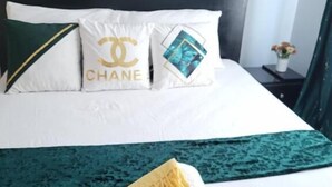 A hotel room with a bed, white bedding, a black headboard, and two pillows with logos. - Lux Suites Supaboma Apartments Embakasi (Nairobi)