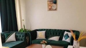 A living room with a green sofa, a coffee table, a white chair, and a small table with a vase. - Lux Suites Supaboma Apartments Embakasi (Nairobi)