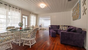 A spacious living room with a glass dining table, white wicker chairs, a purple sofa, and a globe on the table. - Pet Friendly Stuart Oasis Beach House (Stuart)