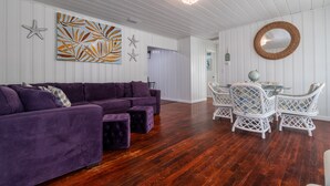 A room with a purple sectional sofa, white wicker chairs, and a dining table. - Pet Friendly Stuart Oasis Beach House (Stuart)