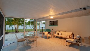 A spacious room with a glass table and chairs, a wooden sofa, and a view of the beach and palm trees. - Pet Friendly Stuart Oasis Beach House (Stuart)