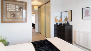 Une chambre à coucher avec un lit, une commode, un tableau encadré et un miroir.