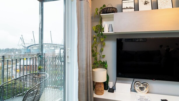 Un salon moderne doté d’un grand téléviseur, d’un canapé, d’un fauteuil et d’un balcon offrant une vue sur un stade.