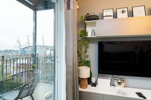 A modern living room with a large TV, a sofa, a chair, and a balcony with a view of a stadium. - Manchester City Football Stadium View (Manchester)