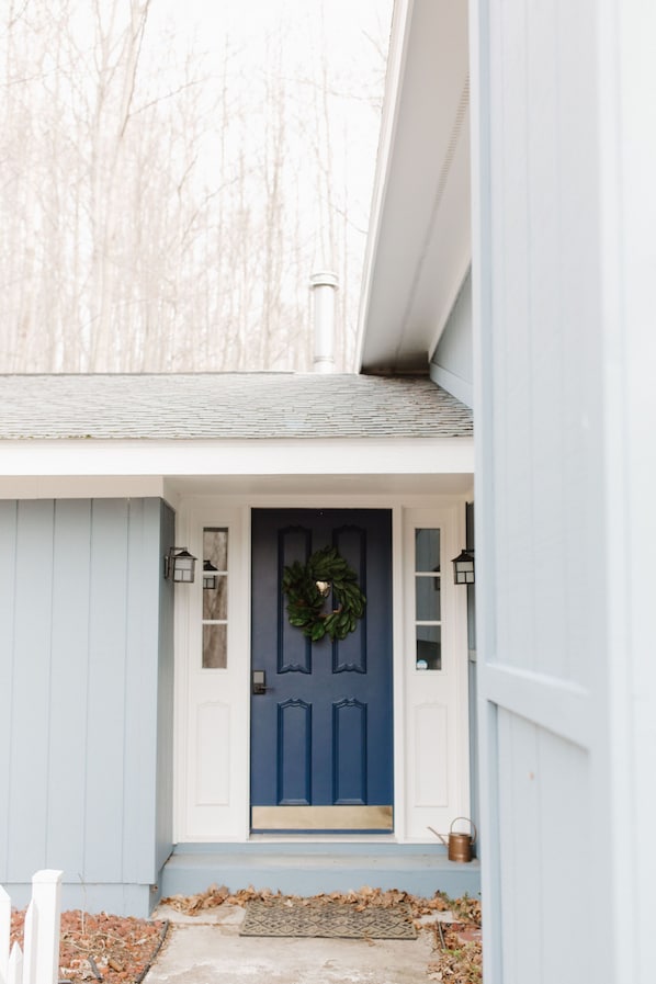 Une maison avec une porte d’entrée bleue, une guirlande et un petit jardin entouré d’une clôture en bois peinte en blanc.