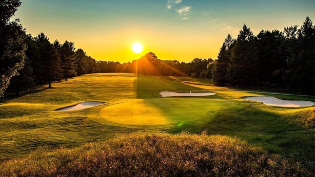 Ein Golfplatz bei Sonnenuntergang mit Sandbunkern und Bäumen.