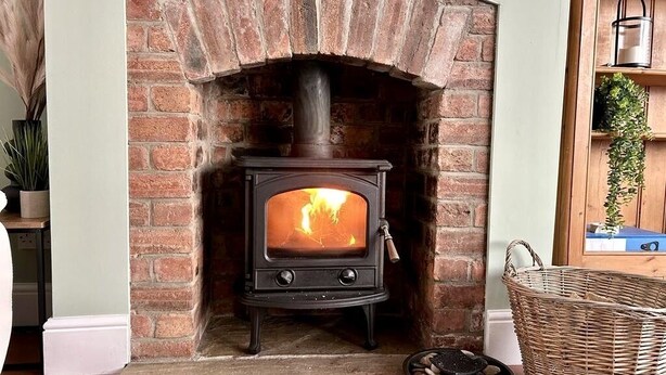 A traditional brick fireplace with a wood-burning stove, a stone hearth, and a wicker basket nearby. - 6 Guests - 3 Bed House in Chester-le-street (Chester-le-Street)