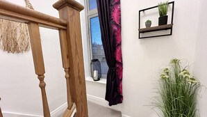 A staircase with wooden handrails, a window with blinds, a dark curtain, and a small shelf with plants. - 6 Guests - 3 Bed House in Chester-le-street (Chester-le-Street)
