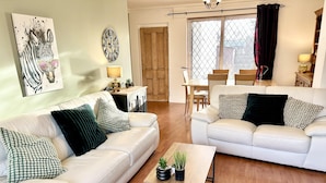 A living room with two white leather sofas, a coffee table, and a dining area with a wooden table and chairs. - 6 Guests - 3 Bed House in Chester-le-street (Chester-le-Street)