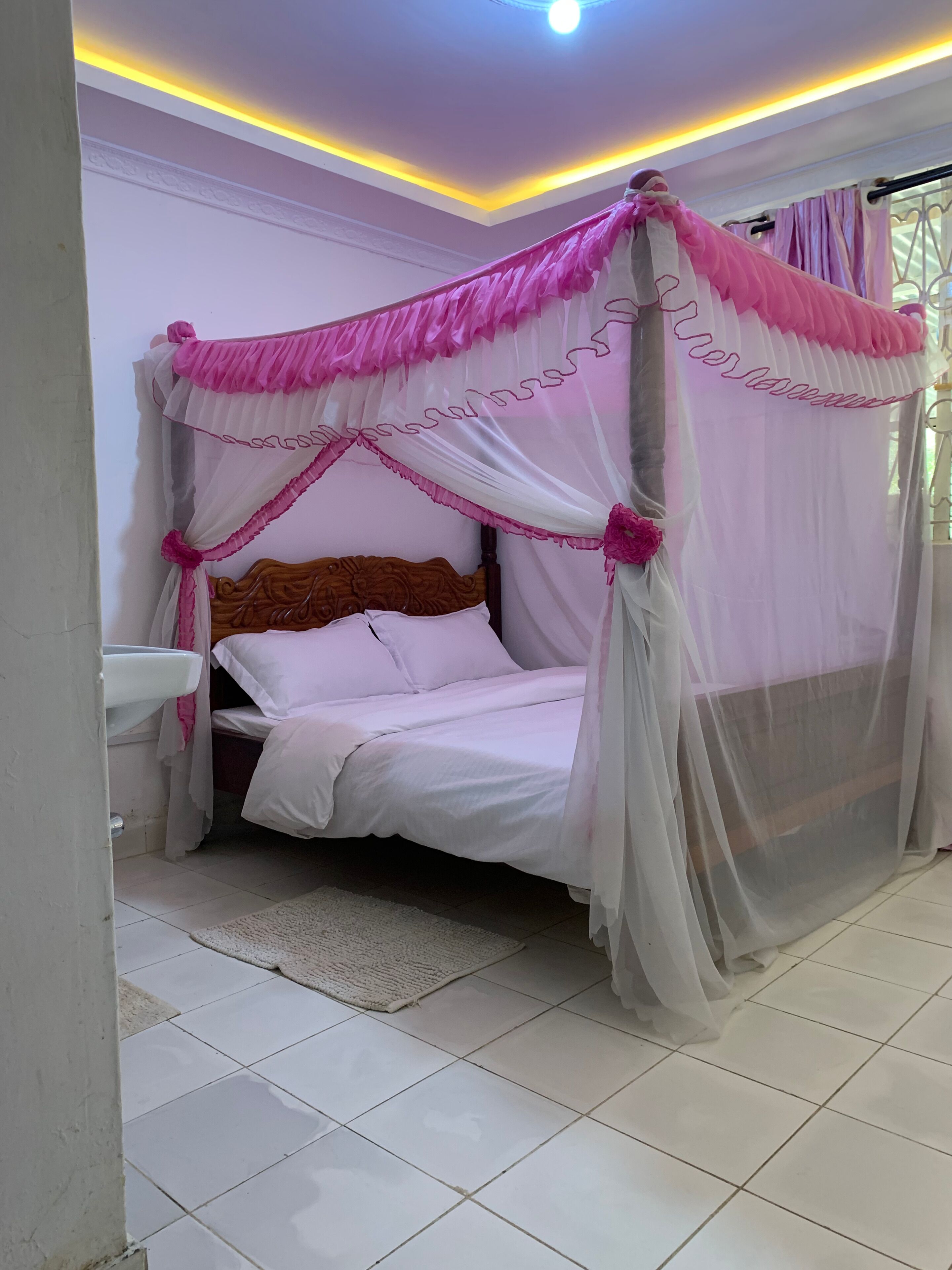A bedroom with a canopy bed, a bedside table, and a window with curtains.