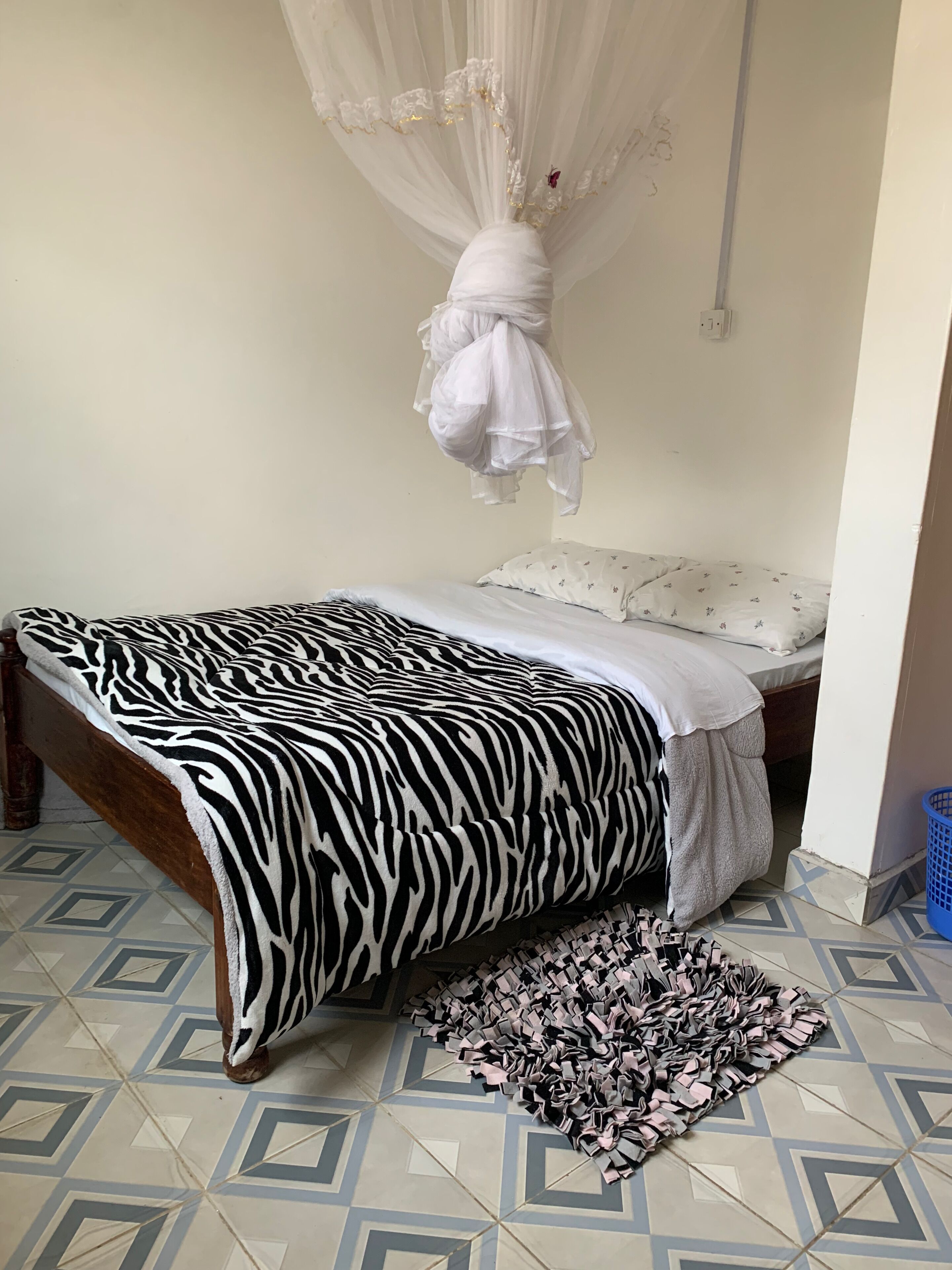 Un dormitorio con una colcha de estampado de cebra, una cama con dosel blanco, una alfombra estampada y un cesto de ropa azul.
