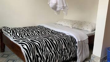 Un dormitorio con una colcha de estampado de cebra, una cama con dosel blanco, una alfombra estampada y un cesto de ropa azul.