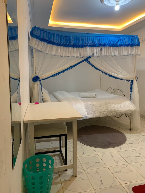 Una habitación con una cama, una mesa, una cesta verde y una lámpara en el techo.