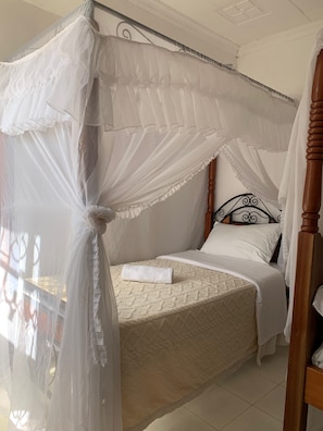 Una cama con dosel, cabecera de madera y cubrecama blanco.