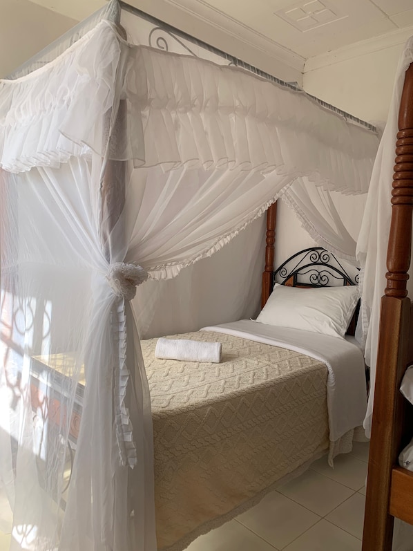A bed with a canopy, a wooden headboard, and a white bedspread. - Nairobi Transit Lounge (Syokimau)