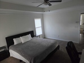 A bedroom with a bed, a ceiling fan, a window with blinds, and a door leading to another room.