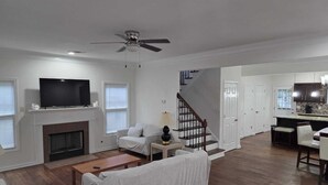 A spacious living room with a fireplace, a sofa, a TV, and a staircase leading to a kitchen.