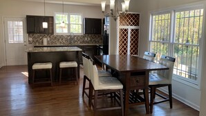 A spacious kitchen with a central island, dark cabinets, and a large dining table with chairs.