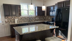 A kitchen with dark wood cabinets, a granite countertop, a black refrigerator, and a window with a view of greenery.