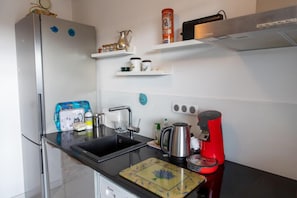 Eine Küche mit Kühlschrank, Spüle, Kaffeemaschine und verschiedenen Küchenutensilien in Regalen.