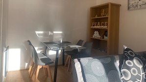 A dining area with a table and chairs, a bookshelf with decorative items, and a wall with a framed picture. - Immaculate 2-bed Villa in Shrewsbury (Shrewsbury)