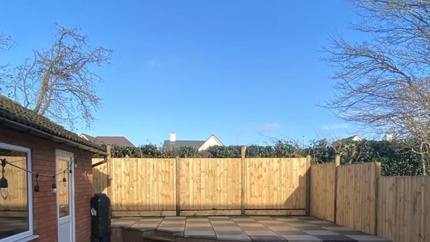 A patio with a checkered tile floor, a wooden fence, and a brick building with a door. - Immaculate 2-bed Villa in Shrewsbury (Shrewsbury)