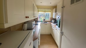 A compact kitchen with white cabinets, a microwave, a stove, and a window with a view of greenery outside. - Immaculate 2-bed Villa in Shrewsbury (Shrewsbury)
