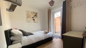 A bedroom with a bed, a small desk, a chair, a painting on the wall, and a view of the outside through a sliding door. - Immaculate 2-bed Villa in Shrewsbury (Shrewsbury)