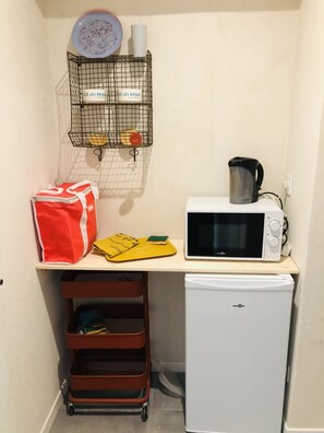 Compact kitchenette with microwave, refrigerator, and storage cart.