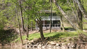 A cabin with a deck overlooking a lake, surrounded by trees. - Triplett Creek Cabin Rental with Scenic Views  – Near Cave Run Lake! (Morehead)