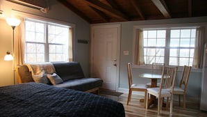 A cozy room with a bed, a sofa, a dining table with chairs, and large windows. - Triplett Creek Cabin Rental with Scenic Views  – Near Cave Run Lake! (Morehead)