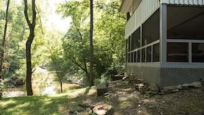 A building with large windows overlooking a forested area with a stream. - Triplett Creek Cabin Rental with Scenic Views  – Near Cave Run Lake! (Morehead)