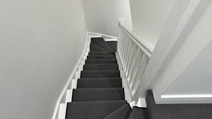 Un escalier avec une rampe blanche et des marches recouvertes d’une moquette sombre.