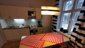A kitchen with a red and white checkered tablecloth, two red chairs, a stove, a microwave, and a window with black and white curtains. - Beautiful 2 Bed Apartment Sauna Facility in Kotka (Kotka)