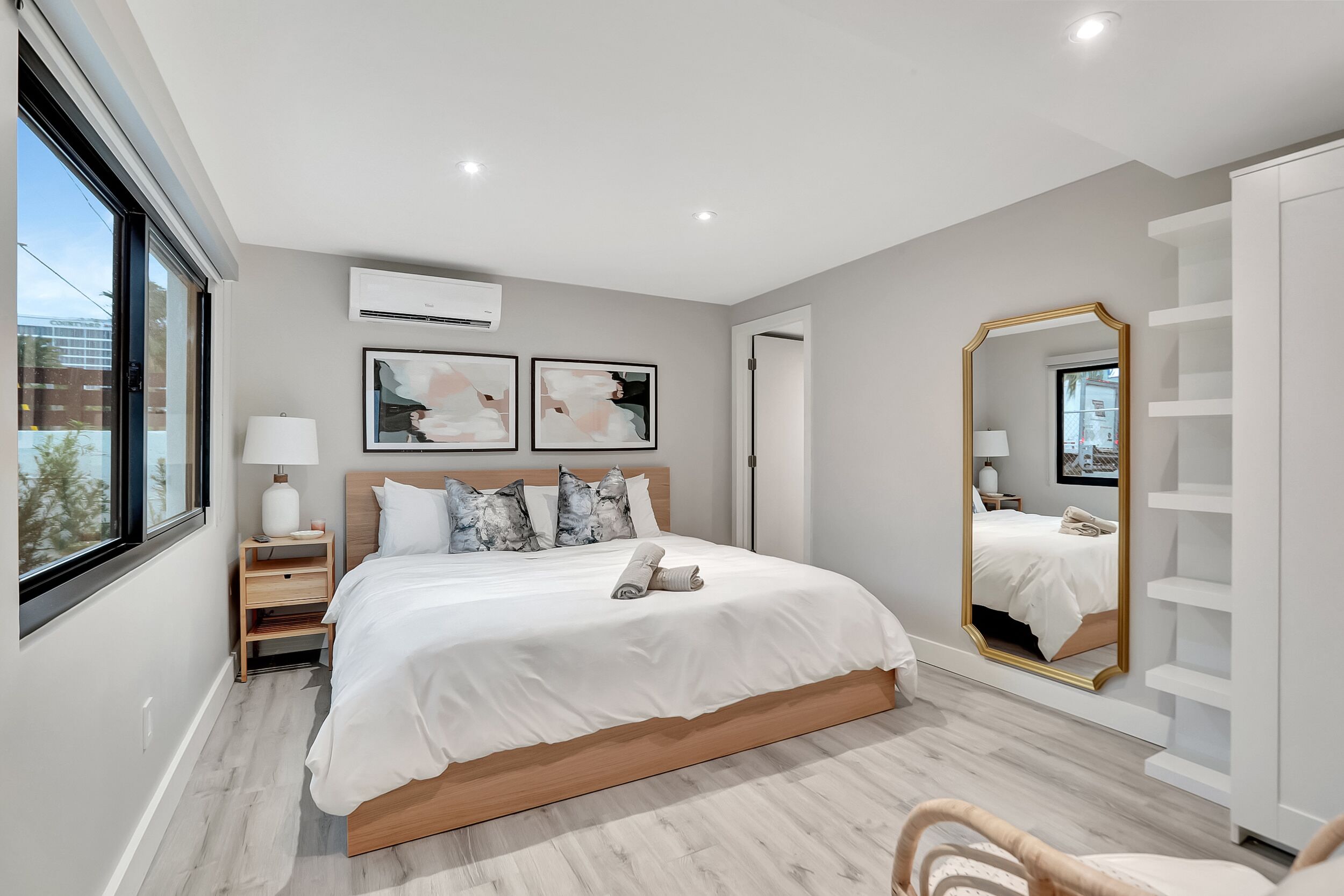 A modern bedroom with a large bed, bedside tables, a mirror, and a view of the outdoors.