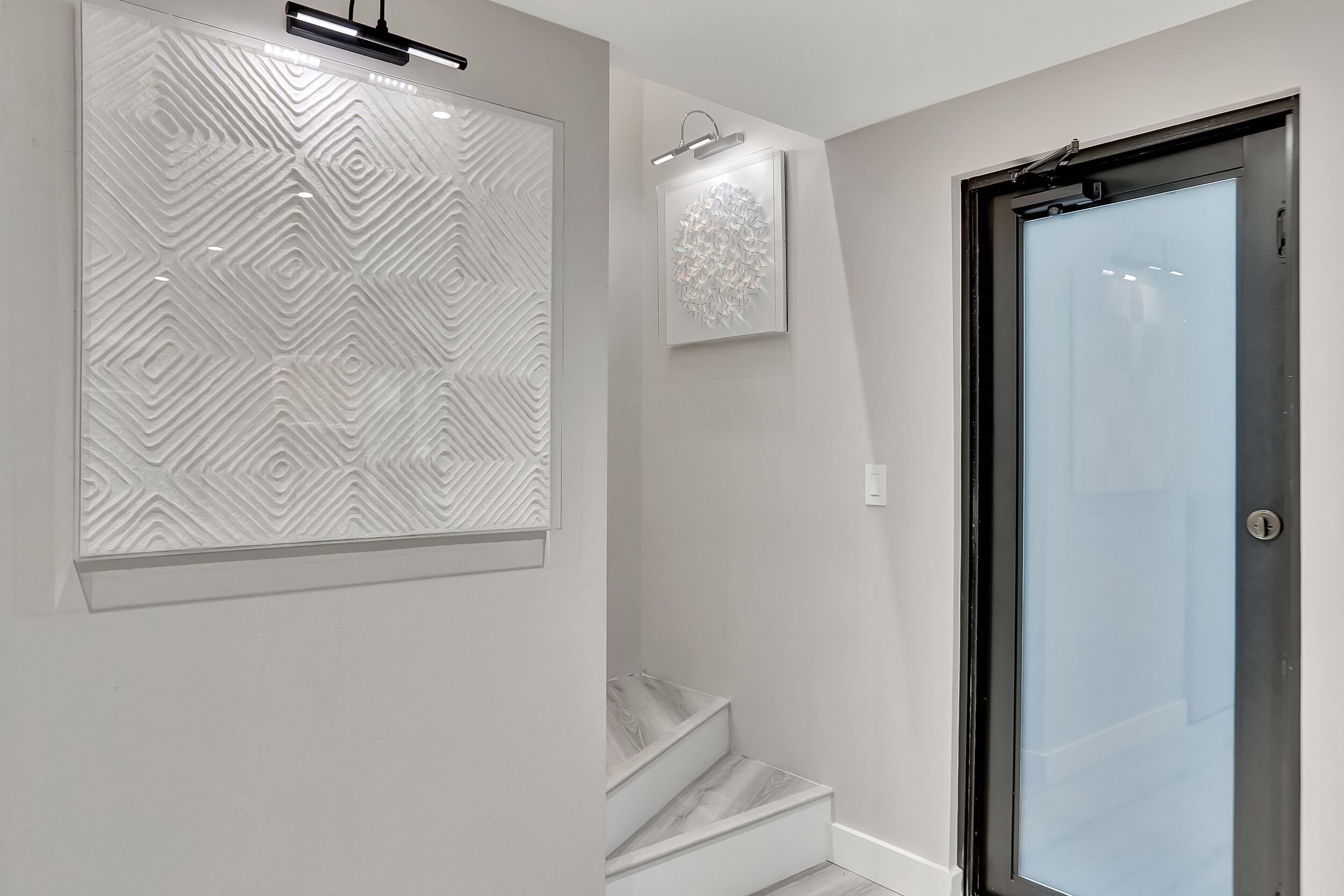 Un intérieur moderne avec un mur orné d’un motif géométrique, une porte en verre et un escalier.