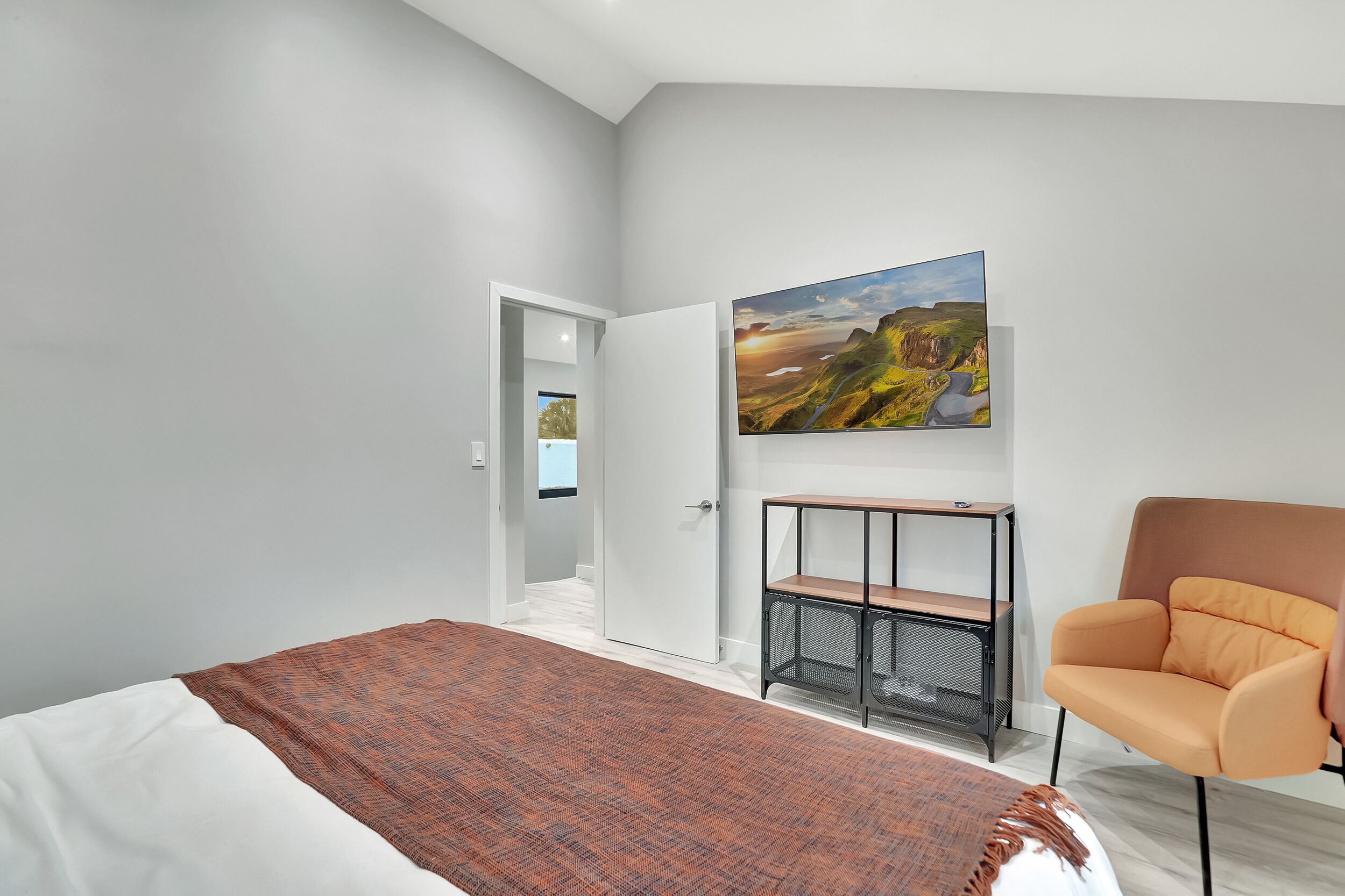 A modern bedroom with a bed, a chair, a desk, and a painting on the wall.