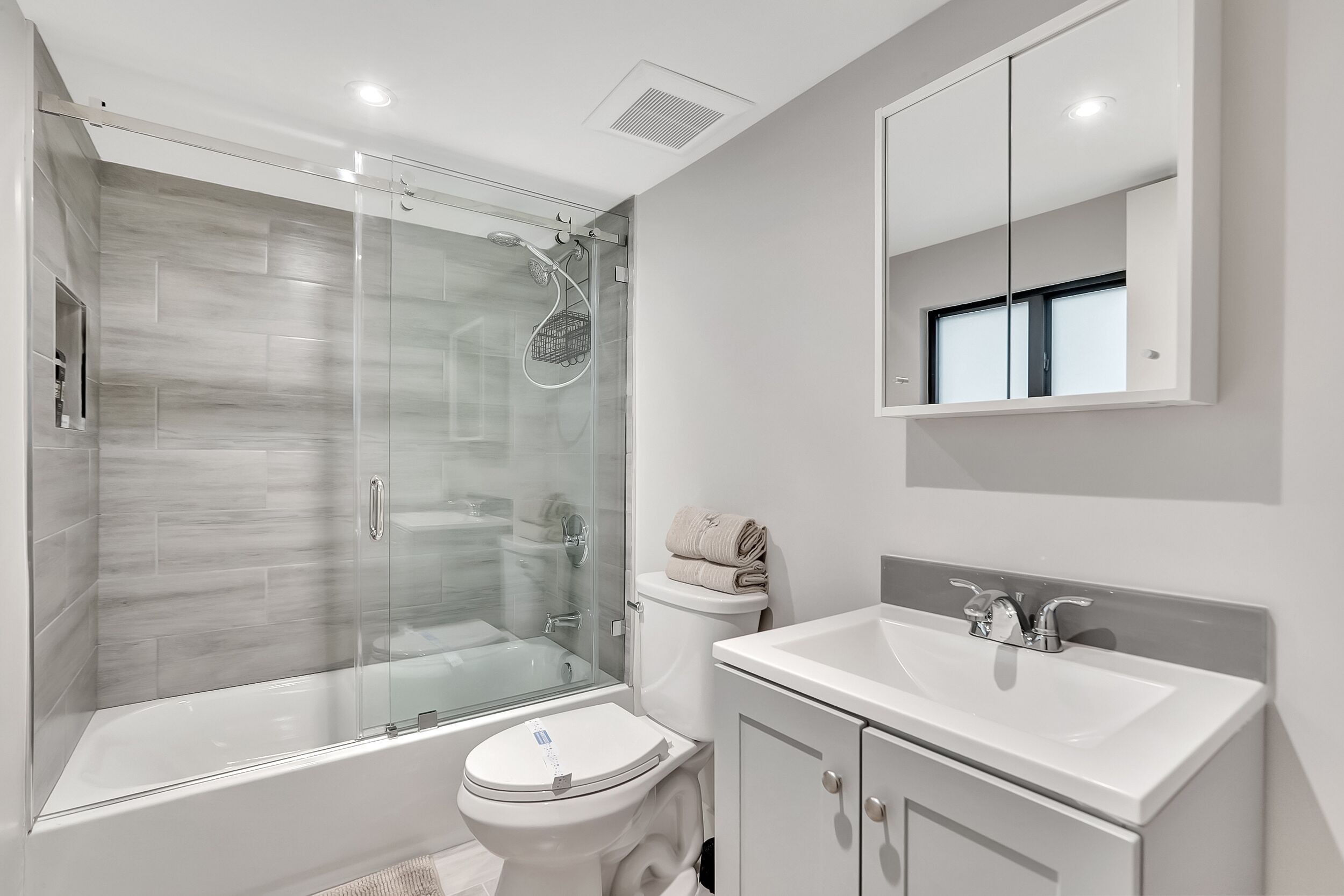 Een moderne badkamer met een douchecabine van glas, een wit toilet, een wastafel en een kast.