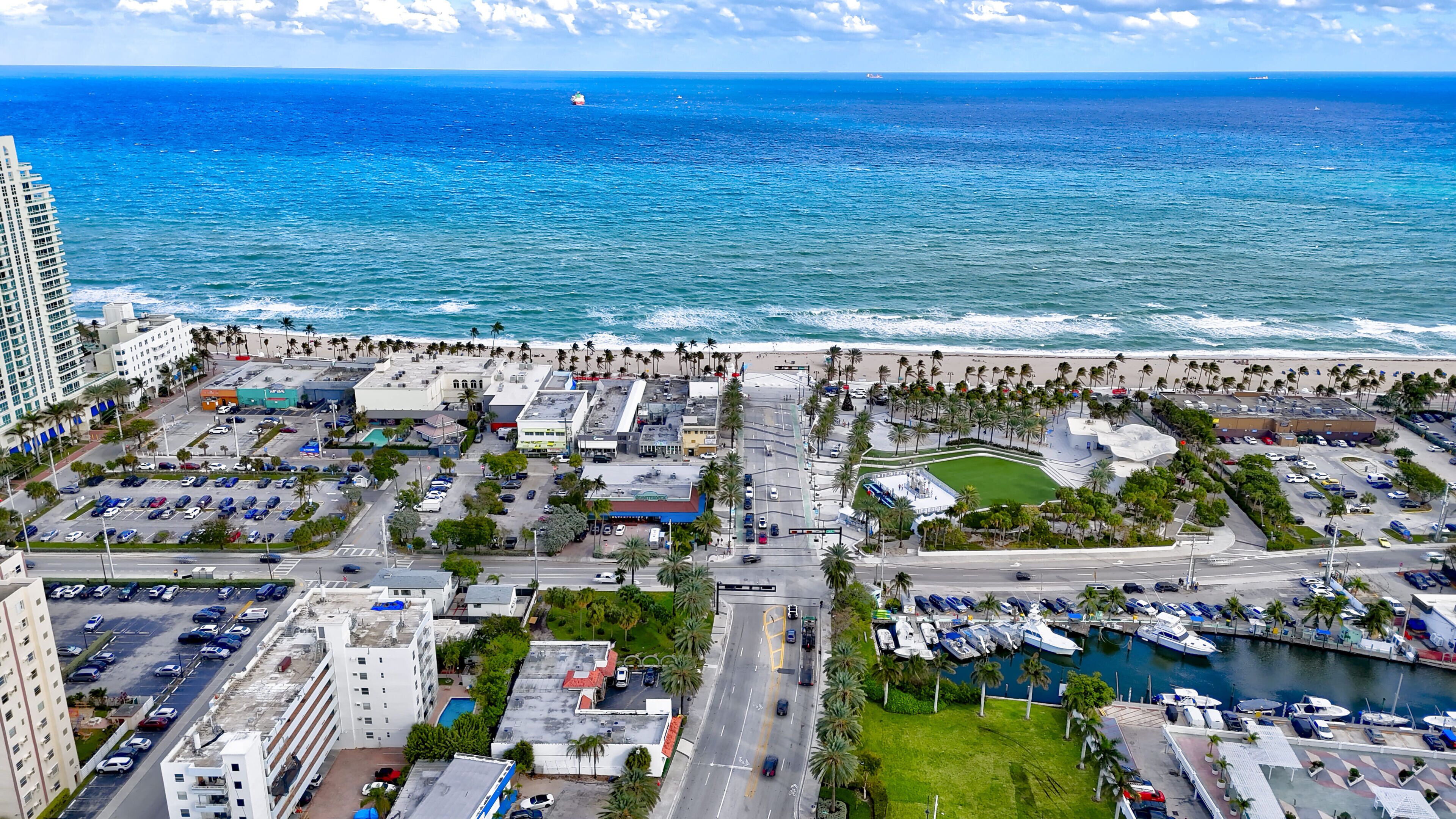An aerial view of a coastal city with a marina, parking areas, and buildings.