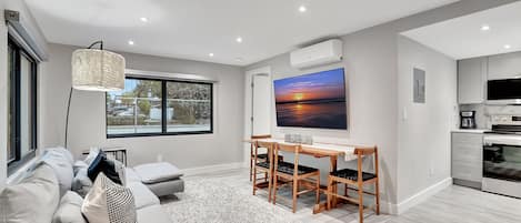 Una sala moderna con un sofá, una mesa de centro, un televisor y un comedor con sillas.