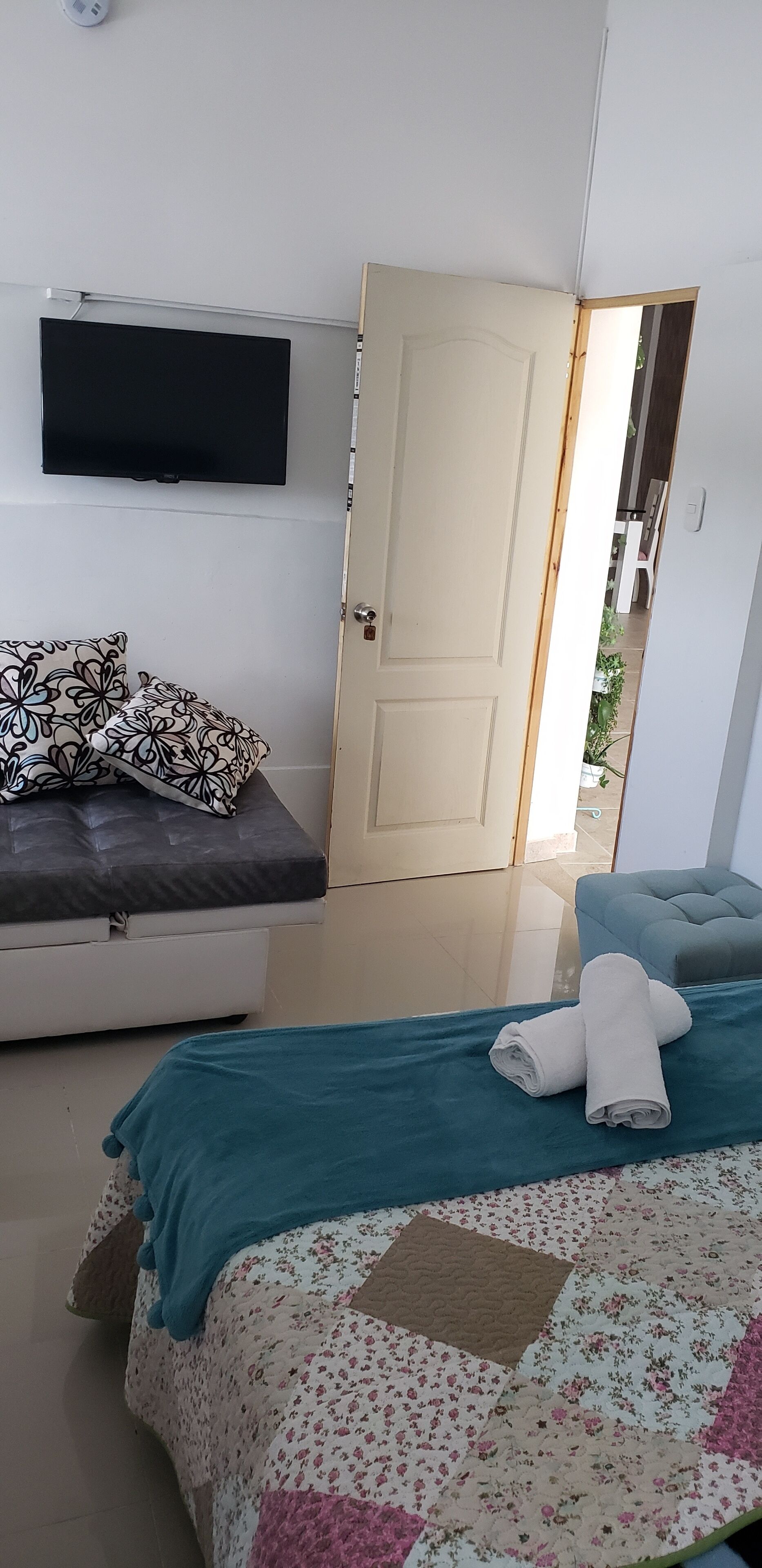 A bedroom with a bed, a sofa, a television, and a door leading to another room.