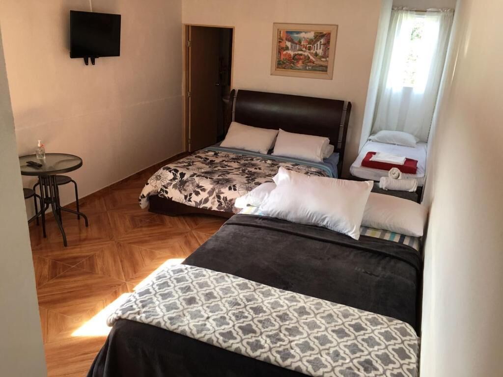 A hotel room with two beds, a small table with a chair, a TV mounted on the wall, and a painting above the bed.