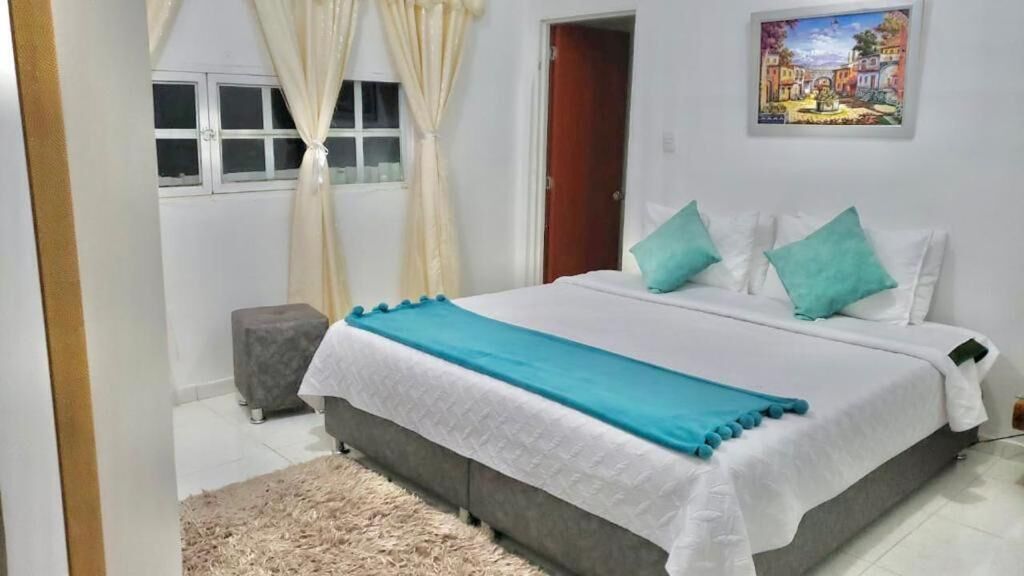 A bedroom with a bed, curtains, a small stool, a painting, and a door.