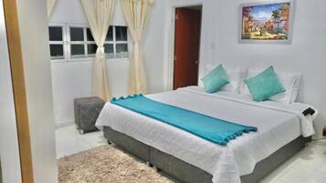A bedroom with a bed, curtains, a small stool, a painting, and a door.
