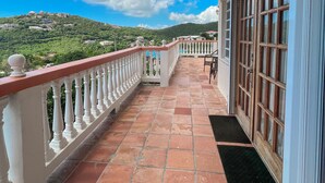 A balcony with a tiled floor, white balustrade, and a view of a hillside with buildings. - New Listing! Island Bliss • 2BR • 3 Beds • 2 Baths (Saint Thomas)